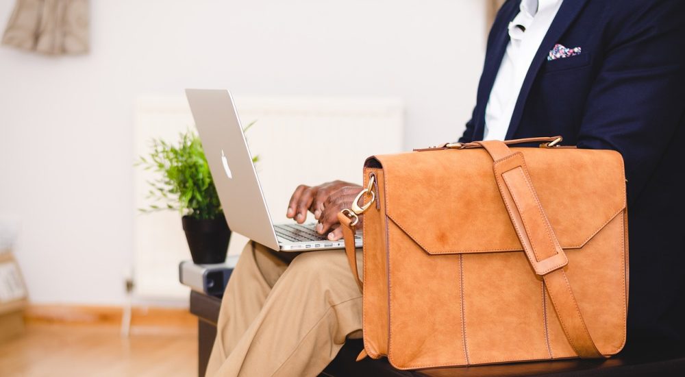 Homme avec une valise qui regarde son ordinateur.
