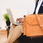Homme avec une valise qui regarde son ordinateur.