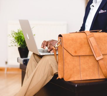 Homme avec une valise qui regarde son ordinateur.