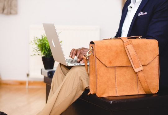 Homme avec une valise qui regarde son ordinateur.